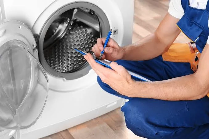 Technician recording diagnostic notes beside a front-loading washing machine